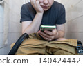 Man sitting on the toilet with a smartphone in hands. Guy scrolling phone on the loo, concept of prolonged sitting risk, screen addiction, and hemorrhoids. Man sitting on the toilet with a smartphone in hands. Guy scrolling phone on the loo, concept of prolonged sitting risk, screen addiction, and hemorrhoids. 140424442