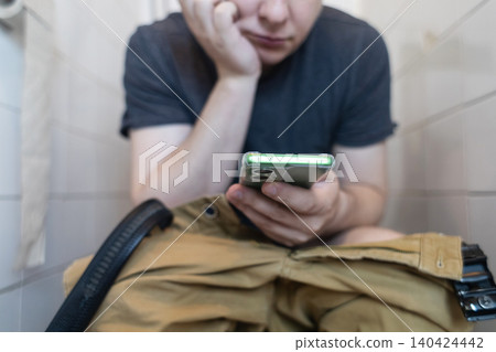 Man sitting on the toilet with a smartphone in hands. Guy scrolling phone on the loo, concept of prolonged sitting risk, screen addiction, and hemorrhoids. Man sitting on the toilet with a smartphone in hands. Guy scrolling phone on the loo, concept of prolonged sitting risk, screen addiction, and hemorrhoids. 140424442