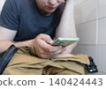 Man sitting on the toilet with a smartphone in hands. Guy scrolling phone on the loo, concept of prolonged sitting risk, screen addiction, and hemorrhoids. Man sitting on the toilet with a smartphone in hands. Guy scrolling phone on the loo, concept of prolonged sitting risk, screen addiction, and hemorrhoids. 140424443
