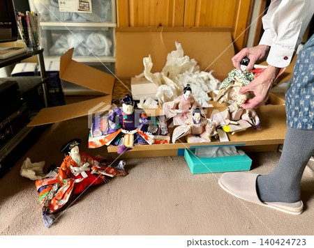 An elderly woman's hands as she puts the Hina dolls into a cardboard box. 140424723