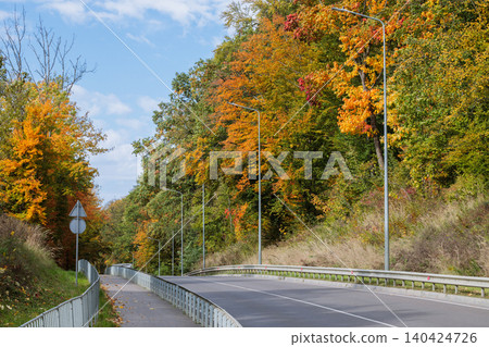 Scenic country road winding through vibrant autumn foliage under a blue sky Scenic country road winding through vibrant autumn foliage under a blue sky 140424726