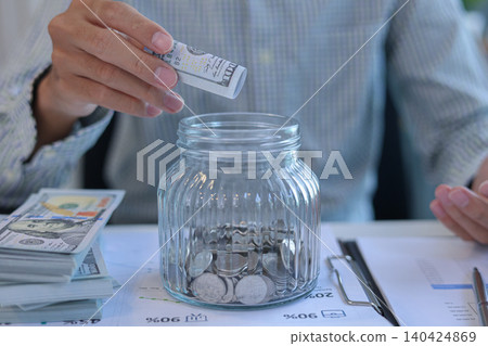 Business Man Putting US Dollar Bill into Saving Jar for Financial Planning and Saving Concept Business Man Putting US Dollar Bill into Saving Jar for Financial Planning and Saving Concept 140424869