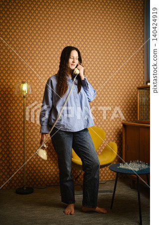 Woman speaking on rotary phone while standing in retro room with chess set Woman speaking on rotary phone while standing in retro room with chess set 140424919