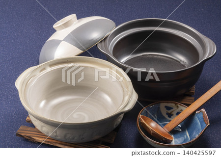 一張日本餐具的產品照片，照片中展示了一個黑白陶罐、一把木勺和一個小盤子，背景是深藍色。 140425597