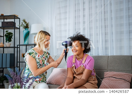 Mother drying smiling daughter's curly hair at home 140426587