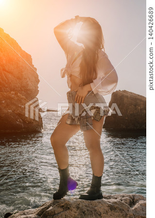 Woman sunset coast posing on a rocky beach wearing a white linen shirt and denim skirt during a golden hour evening Woman sunset coast posing on a rocky beach wearing a white linen shirt and denim skirt during a golden hour evening 140426689