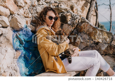 Woman cat cuddle holding a feline friend while sitting on a bench by a rocky cliff under the sun Woman cat cuddle holding a feline friend while sitting on a bench by a rocky cliff under the sun 140426718