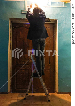 Man on ladder inspecting or replacing a light bulb above front door entrance Man on ladder inspecting or replacing a light bulb above front door entrance 140426875