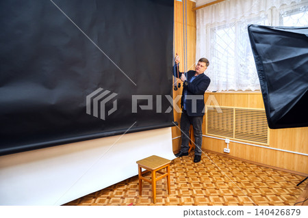 Male photographer lowering a black backdrop for a photo shoot in a professional studio setting Male photographer lowering a black backdrop for a photo shoot in a professional studio setting 140426879
