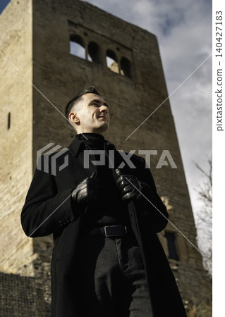 Confident Man in Black Coat Near Stone Tower 140427183