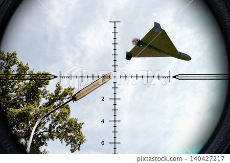 Strike drone appears in optical scope view above urban infrastructure and observation targets. Strike drone appears in optical scope view above urban infrastructure and observation targets. 140427217