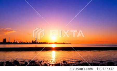 A silhouette landscape of the seaside and factories bathed in the setting sun. 140427348