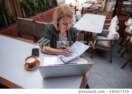 Woman writing in notebook while working remotely at cafe 140427358