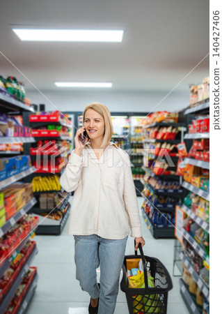 Woman talking on phone while grocery shopping in supermarket aisle Woman talking on phone while grocery shopping in supermarket aisle 140427406