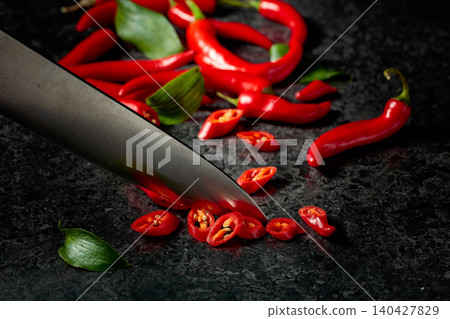 Kitchen knife and slices of red hot chili peppers on a kitchen table. Kitchen knife and slices of red hot chili peppers on a kitchen table. 140427829