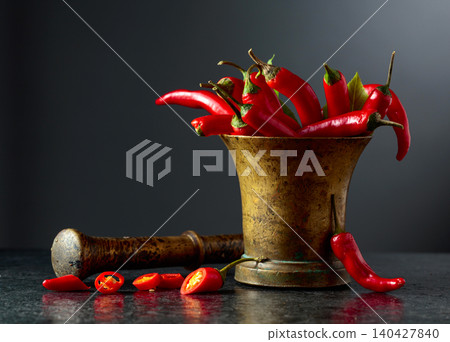 Fresh red chili peppers in old brass mortar on a black table. Fresh red chili peppers in old brass mortar on a black table. 140427840