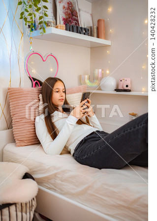 Teenage girl relaxing on bed using smartphone 140428232