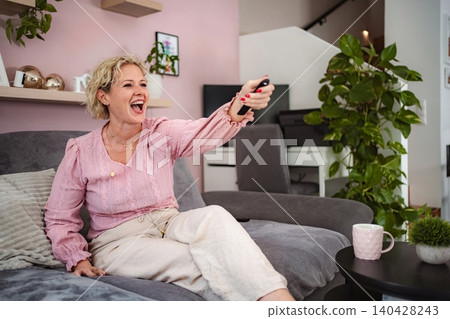 Woman laughing watching TV holding remote control on couch 140428243