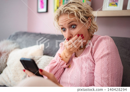 Woman receiving shocking news on smartphone at home Woman receiving shocking news on smartphone at home 140428294