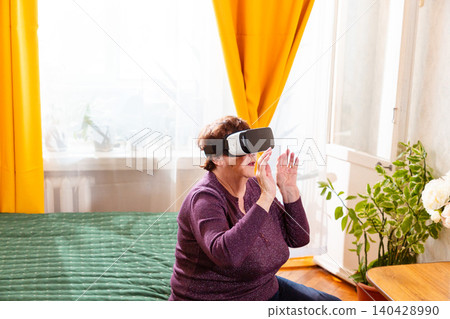 Elderly woman testing virtual reality headset and exploring digital world indoors. Smart technology and future living concept. Active retirement and innovation engagement. Elderly woman testing virtual reality headset and exploring digital world indoors. Smart technology and future living concept. Active retirement and innovation engagement. 140428990
