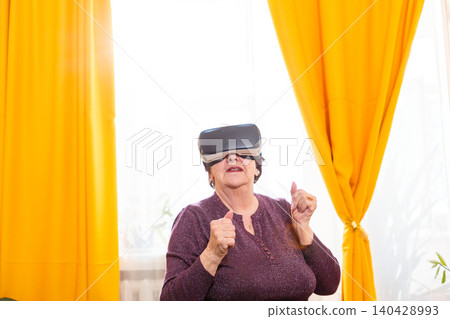 Elderly woman wearing VR headset and exploring immersive environment. Digital lifestyle concept. Lifelong learning and curiosity. Copy space Elderly woman wearing VR headset and exploring immersive environment. Digital lifestyle concept. Lifelong learning and curiosity. Copy space 140428993