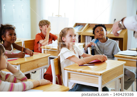 Diverse elementary school children listening to teacher in classroom 140429386
