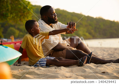 African American father and son watching sunset on the beach 140429441