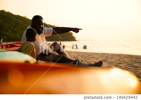 African American father and son watching sunset on the beach 140429442