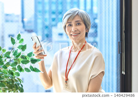 一位頭髮花白的女士一邊拿著智慧型手機,一邊愉快地交談。 一位頭髮花白的女士一邊拿著智慧型手機,一邊愉快地交談。 140429486