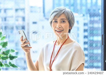 一位頭髮花白的女士面帶微笑，拿著智慧型手機撥打電話。 140429487