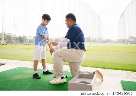 Young boy practicing golf swing with professinoal golf instructor at driving range 140429505