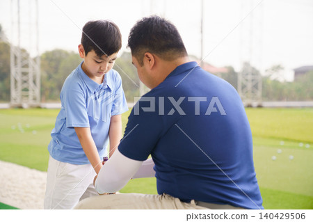 Young boy practicing golf swing with professinoal golf instructor at driving range Young boy practicing golf swing with professinoal golf instructor at driving range 140429506