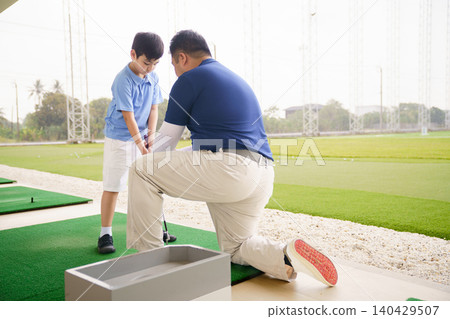 Young boy practicing golf swing with professinoal golf instructor at driving range Young boy practicing golf swing with professinoal golf instructor at driving range 140429507