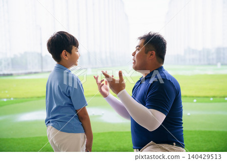 Young boy practicing golf swing with professinoal golf instructor at driving range Young boy practicing golf swing with professinoal golf instructor at driving range 140429513