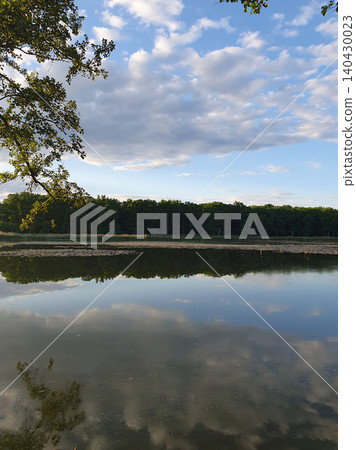 Picturesque summer landscape: mirror lake with reeds, reflection of clouds in the water, green forest on the horizon Picturesque summer landscape: mirror lake with reeds, reflection of clouds in the water, green forest on the horizon 140430023