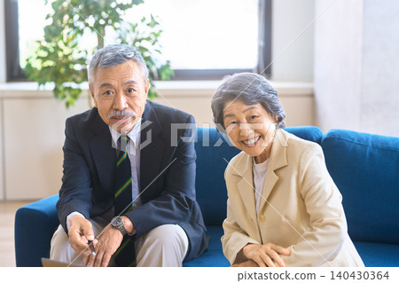 一位老年男子和一位微笑的女子坐在沙發上看向鏡頭。 140430364