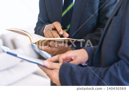 一名男子一邊看著平板電腦,一邊在筆記本上做筆記。 一名男子一邊看著平板電腦,一邊在筆記本上做筆記。 140430369
