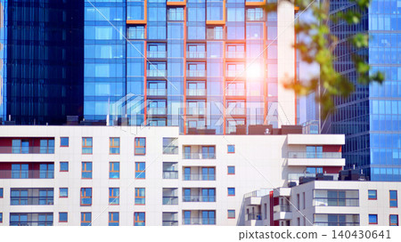 A low-rise residential building stands against a backdrop of tall glass buildings. An urban quarter of modern architecture. A low-rise residential building stands against a backdrop of tall glass buildings. An urban quarter of modern architecture. 140430641