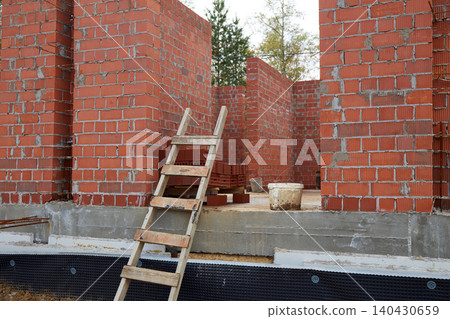 Entrance area of an unfinished brick building with wooden ladder, construction buckets, and stacked masonry blocks 140430659