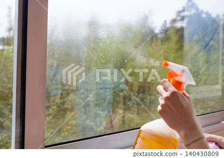 A person sprays cleaning liquid onto a dirty window using a spray bottle while preparing to wipe the glass surface A person sprays cleaning liquid onto a dirty window using a spray bottle while preparing to wipe the glass surface 140430809