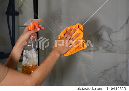 Hands cleaning a glass shower door with spray bottle and microfiber cloth removing water spots and soap residue Hands cleaning a glass shower door with spray bottle and microfiber cloth removing water spots and soap residue 140430823
