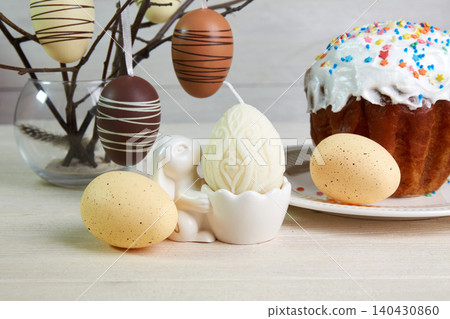 The table is decorated with Easter decorations: colorful eggs, a candle, and an Easter cake covered in icing. The table is decorated with Easter decorations: colorful eggs, a candle, and an Easter cake covered in icing. 140430860