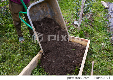 Gardener moves soil using a wheelbarrow in a garden during daytime Gardener moves soil using a wheelbarrow in a garden during daytime 140430971