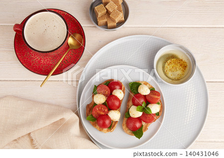 Bruschetta Caprese with mozzarella, cherry tomatoes, and basil on a plate. A cup of coffee and sugar nearby. Bruschetta Caprese with mozzarella, cherry tomatoes, and basil on a plate. A cup of coffee and sugar nearby. 140431046