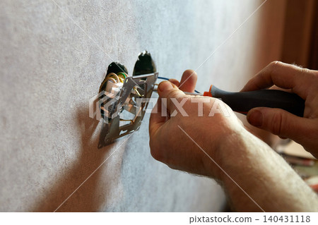 A worker installs an electrical outlet into a wall using a screwdriver A worker installs an electrical outlet into a wall using a screwdriver 140431118