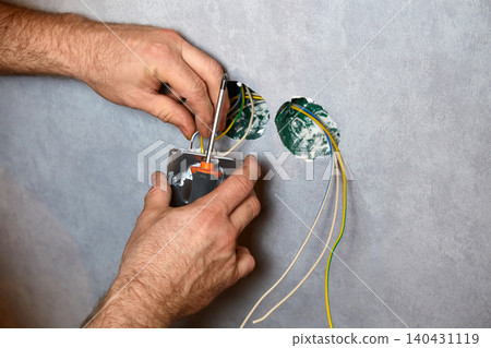 A worker installs an electrical outlet into a wall using a screwdriver A worker installs an electrical outlet into a wall using a screwdriver 140431119