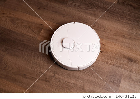 A robot vacuum cleaner moves across the wooden floor in the living room. A robot vacuum cleaner moves across the wooden floor in the living room. 140431123