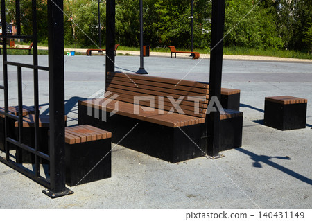 Brown wooden benches are arranged in an outdoor park setting with no people present. Brown wooden benches are arranged in an outdoor park setting with no people present. 140431149