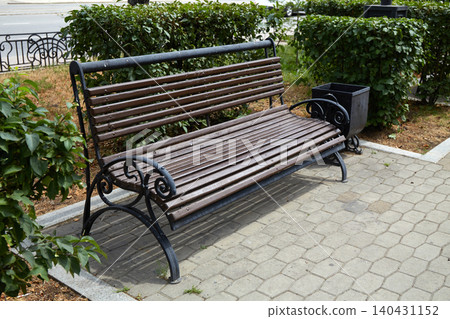 A wooden bench made of slats rests on a stone pathway in a park. A wooden bench made of slats rests on a stone pathway in a park. 140431152