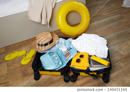 Colorful summer essentials including a sun hat, sandals, and a swim ring are neatly packed in a suitcase Colorful summer essentials including a sun hat, sandals, and a swim ring are neatly packed in a suitcase 140431169